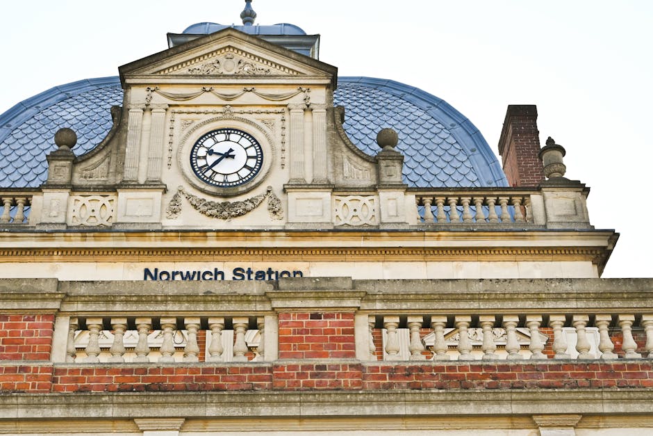 The image shows a multi-storey red brick building with distinctive turreted towers topped with conical grey roofs, situated at a street corner. The building features large windows with white frames an